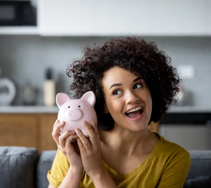 Woman Smiling And Listening To The Jingle Of Money In Her Piggy Bank